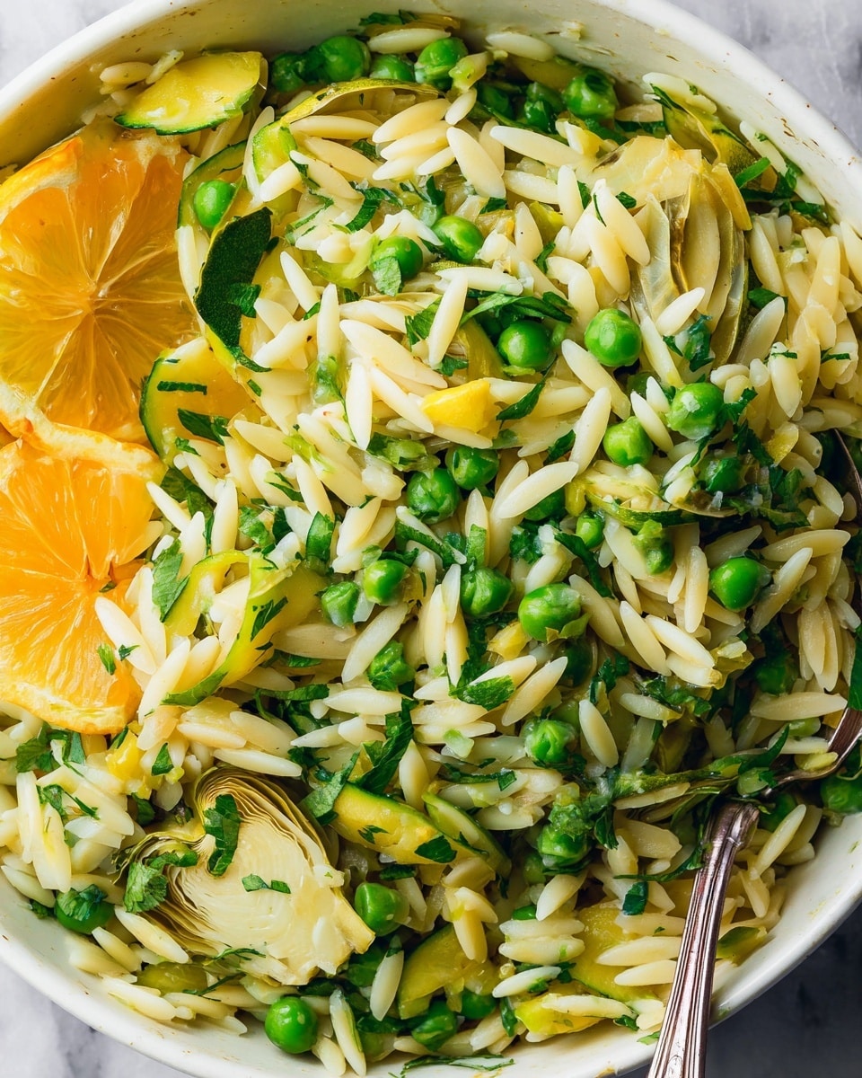 A close-up view of a white bowl filled with orzo pasta mixed with bright green peas, sliced artichoke hearts, and thin strips of green zucchini. There are scattered pieces of fresh green herbs throughout the dish, adding a touch of color and texture. Half a lemon, showing its juicy orange-yellow flesh, sits on the left side inside the bowl. The orzo looks lightly cooked, with a slightly glossy texture. A shiny silver spoon is partially visible on the right edge of the bowl, resting inside the mixture. The bowl sits on a white marbled surface. photo taken with an iphone --ar 4:5 --v 7