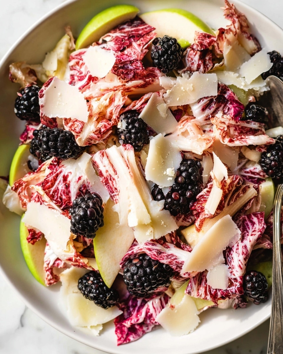 A white bowl filled with a layered salad starting with thin slices of green apple as the base, topped with bright red and white radicchio leaves that add a rough, crinkled texture, scattered juicy blackberries throughout, and finished with thin, off-white shaved cheese pieces spread unevenly on top. The salad ingredients appear fresh and vibrant against the white marbled surface background, with a metal spoon partially visible on the right side. Photo taken with an iphone --ar 4:5 --v 7