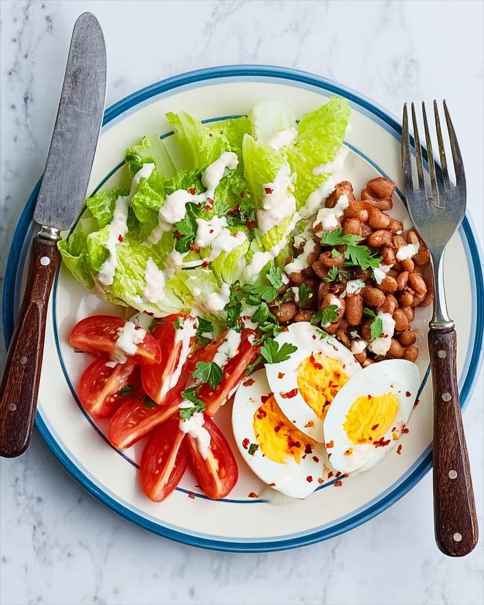 A white plate with a narrow blue rim holds a fresh salad arranged in distinct sections. On the top left, two green lettuce wedges with creamy white dressing drizzled on them. Below the lettuce, bright red tomato wedges form a neat row. To the right of the tomatoes and lettuce, there is a small pile of brown cooked beans topped with some of the same creamy dressing and sprinkled with red chili flakes and green parsley leaves. On the top right of the plate, two halves of a boiled egg with bright yellow yolks are also garnished with red chili flakes and parsley. The plate is set on a white marbled surface with a fork on the left and knife on the right, both with dark wooden handles. Photo taken with an iphone --ar 4:5 --v 7