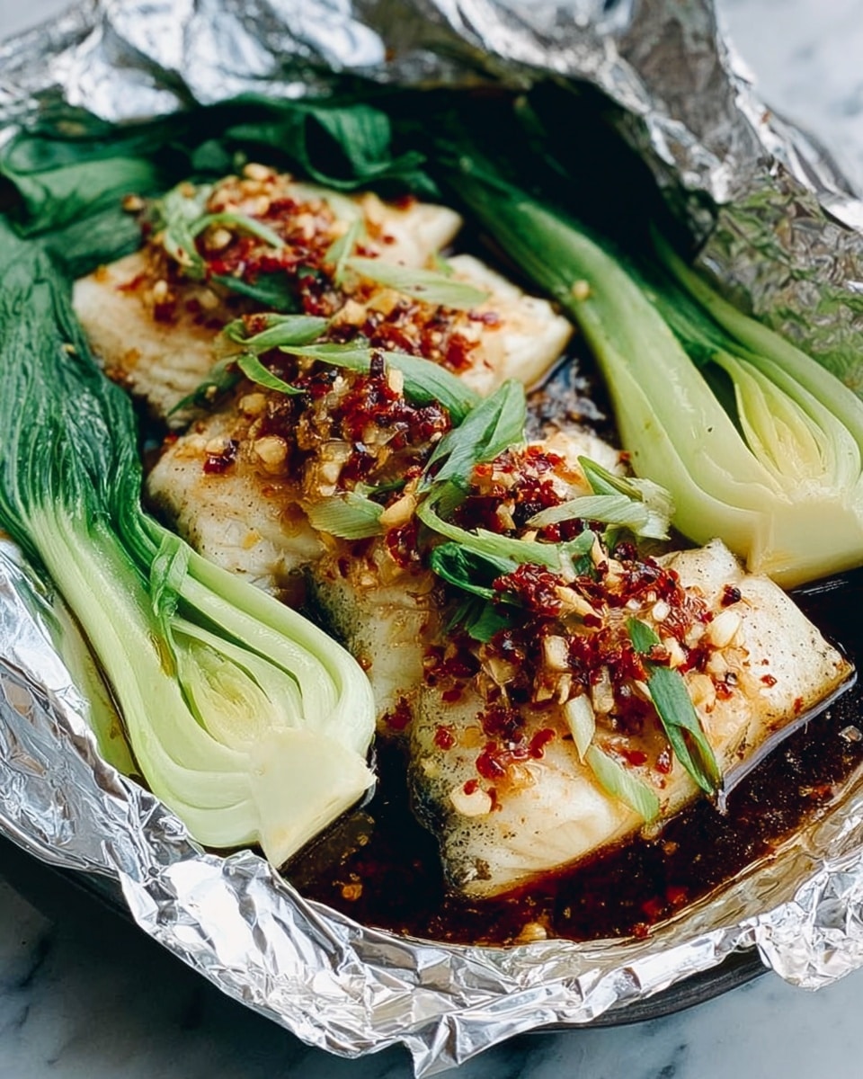 The image shows a foil-lined white plate holding cooked fish fillets topped with finely chopped red and white ingredients, possibly garlic and chili, creating a colorful, textured layer on the fish. Surrounding the fish are several green baby bok choy pieces with pale white stalks, giving a fresh contrast to the dish. The fish sits in a dark sauce pooled in the foil, which reflects light, adding depth. The entire setup rests on a white marbled surface. photo taken with an iphone --ar 4:5 --v 7