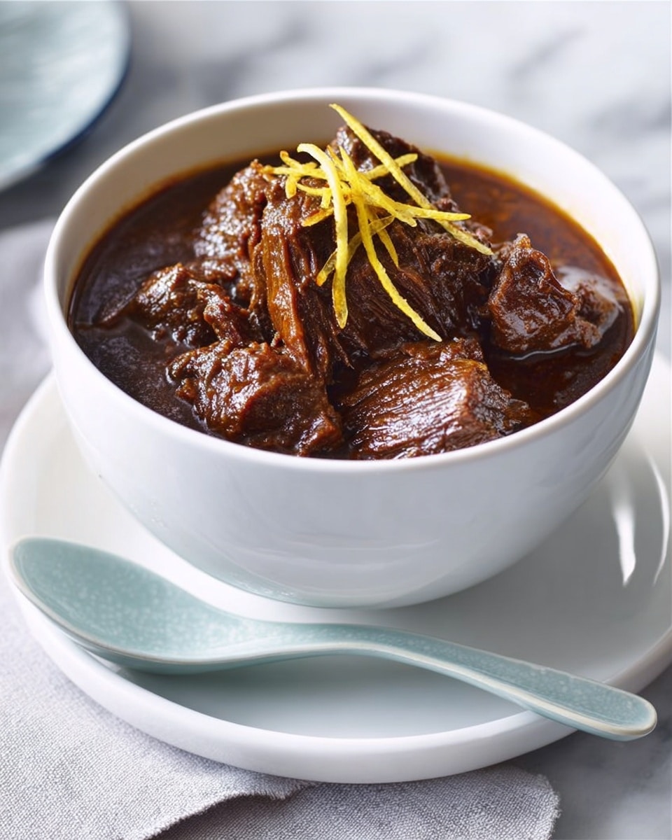 A white bowl filled with rich, dark brown stew that looks thick and tender, with soft meat pieces clearly visible on the top layer. Thin yellow strips, likely ginger, are placed on top as a garnish, adding a touch of bright color to the dish. The bowl sits on a white plate with a light blue ceramic spoon resting on the plate’s edge. The background is a white marbled surface beneath a soft, neutral cloth. Photo taken with an iphone --ar 4:5 --v 7