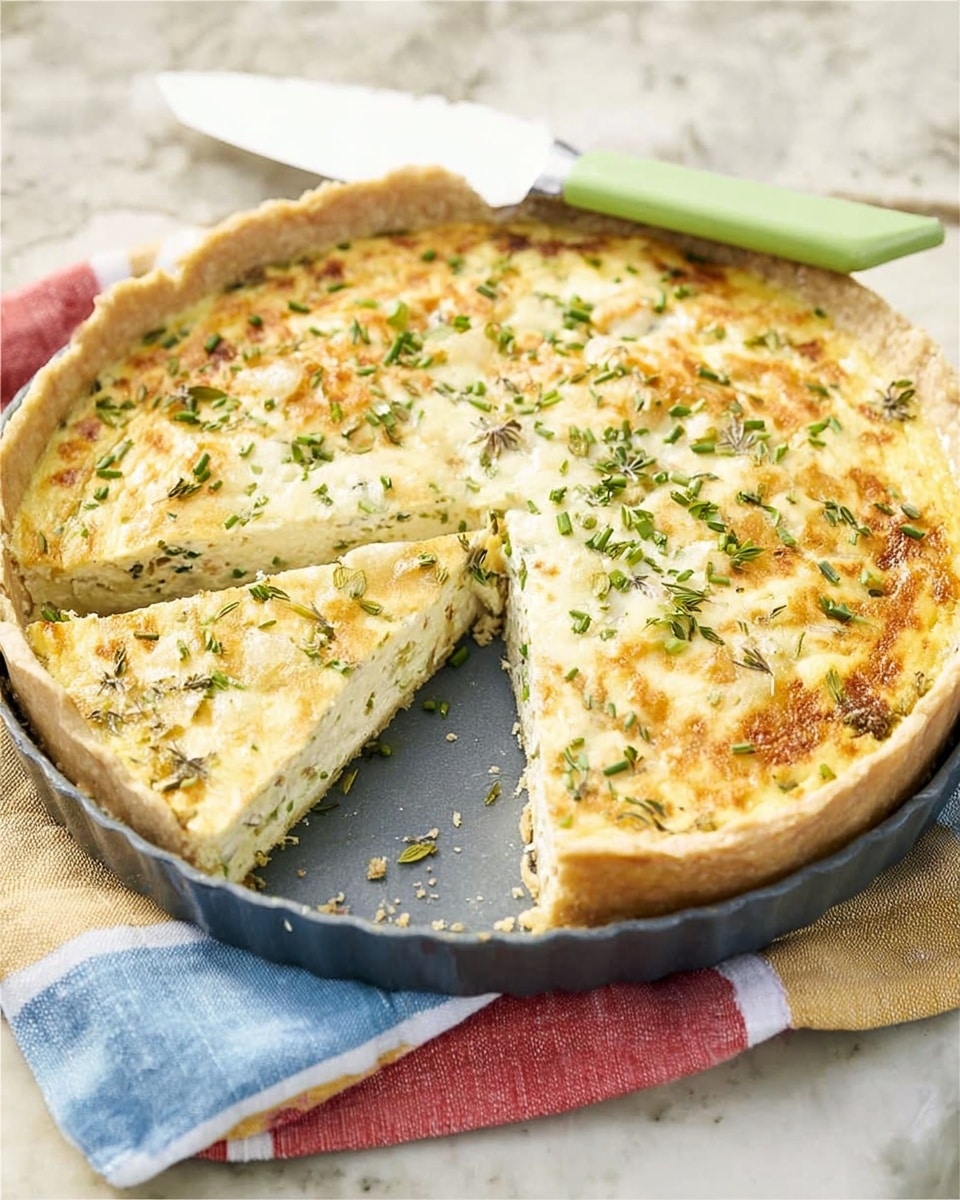 A round savory pie with a golden-brown crust, about one layer thick, sits in a dark gray pie dish. The filling layer is creamy white with small pieces of green herbs and bits of light orange, giving a soft texture on top. One slice has been cut and slightly pulled out, showing the smooth inside. A white knife with a light green handle rests on the edge of the dish. The pie dish is placed on a folded cloth with red, blue, yellow, and white stripes, all set on a white marbled surface. photo taken with an iphone --ar 4:5 --v 7