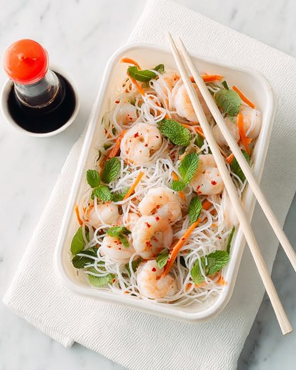 The image shows a white rectangular container filled with a layered shrimp noodle salad. The bottom layer consists of thin white rice noodles, topped with small cooked shrimp that are pale pink with red seasoning specks. Scattered throughout are thin orange carrot strips and light green, leafy herbs, with some darker green mint leaves visible on top. A pair of light wooden chopsticks rests diagonally across the container. To the side, there is a small white round dish holding a dark soy sauce bottle with a red cap. The container sits on a white marbled surface with a white napkin beneath it. Photo taken with an iphone --ar 4:5 --v 7