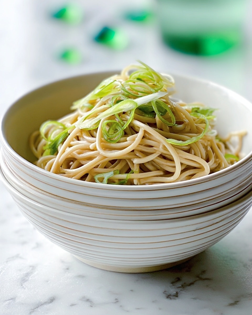 A white bowl filled with light brown noodles piled loosely in the center, topped with thin strips of fresh green onions scattered on top. The bowl has a simple layered design and sits on a white marbled surface with some soft green beads blurred in the background. The noodles look soft and slightly oily, giving a shiny texture, while the green onion adds a crisp, fresh contrast. Photo taken with an iphone --ar 4:5 --v 7