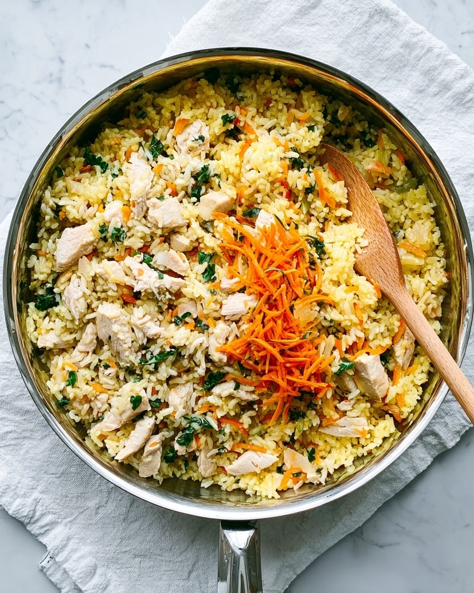 A round silver pan filled with three layers of food is placed on a white cloth over a white marbled surface. The base layer is made up of yellow rice mixed with small bits of green leafy vegetables scattered throughout. The middle layer features small pieces of white chicken scattered unevenly across the rice. On top, there are thin orange carrot strands and more small leafy greens, adding texture and color. A wooden spoon with a smooth handle rests inside the pan, angled toward the right side. Photo taken with an iphone --ar 4:5 --v 7
