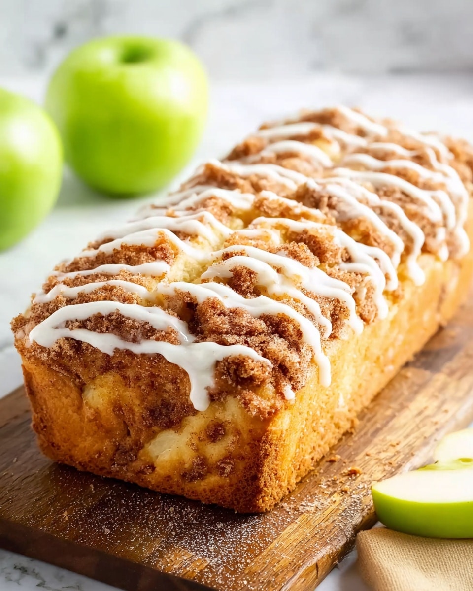 The image shows a rectangular cinnamon roll cake with a golden brown crust and a soft, fluffy texture inside. The cake is topped with a layer of crumbly cinnamon sugar swirl that is darker brown and slightly crispy. On top of the cinnamon layer, there are thin white icing stripes drizzled across lengthwise. The cake rests on a wooden board with a sliced green apple and a whole green apple blurred in the background, all set on a white marbled surface. Photo taken with an iphone --ar 4:5 --v 7