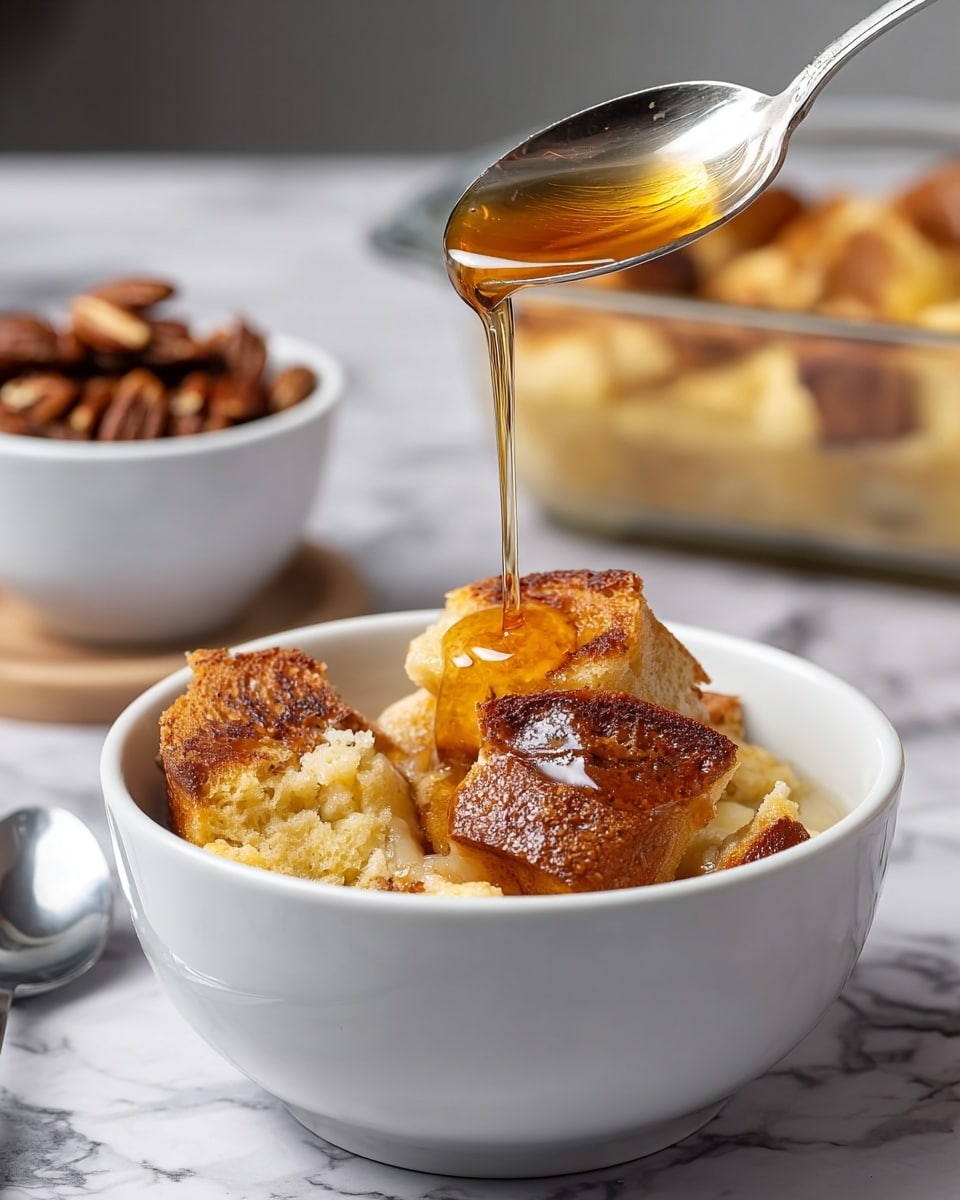 A white bowl filled with three layers of bread pudding: the base layer is soft, moist bread soaked in custard with a light golden color, the middle layer has toasted bread pieces with a crispy light brown crust, and the top layer shows two pieces of toasted bread with golden-brown edges. Golden syrup is being poured over the top, creating a shiny stream and glossy texture on the bread. In the background, there is a clear glass baking dish with more bread pudding and another white bowl containing caramelized pecans or nuts. A silver spoon lies near the bowl on a white marbled surface. photo taken with an iphone --ar 4:5 --v 7