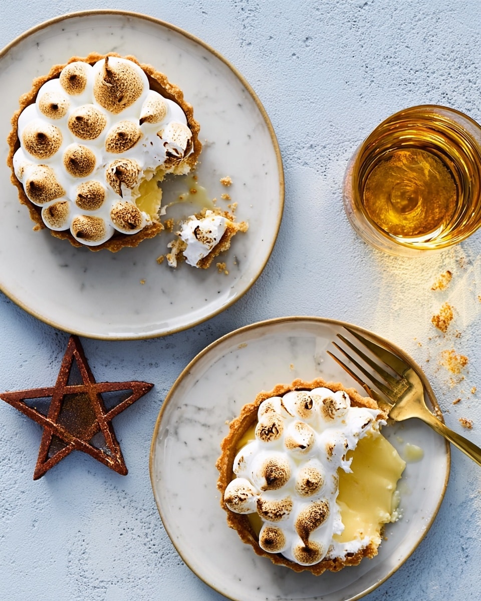 The image shows two small round lemon meringue tarts on separate white plates with a slightly rough texture. Each tart has three layers: a crumbly golden brown crust at the bottom, a smooth pale yellow lemon filling in the middle, and a layer of toasted white meringue shaped into small, round peaks on top, some with light brown spot edges from toasting. One tart is whole, while the other is partially eaten, revealing the glossy lemon filling inside. A copper fork rests on the plate of the partially eaten tart, and a glass of light amber liquid is placed near the top of the frame on a white marbled surface background. photo taken with an iphone --ar 4:5 --v 7
