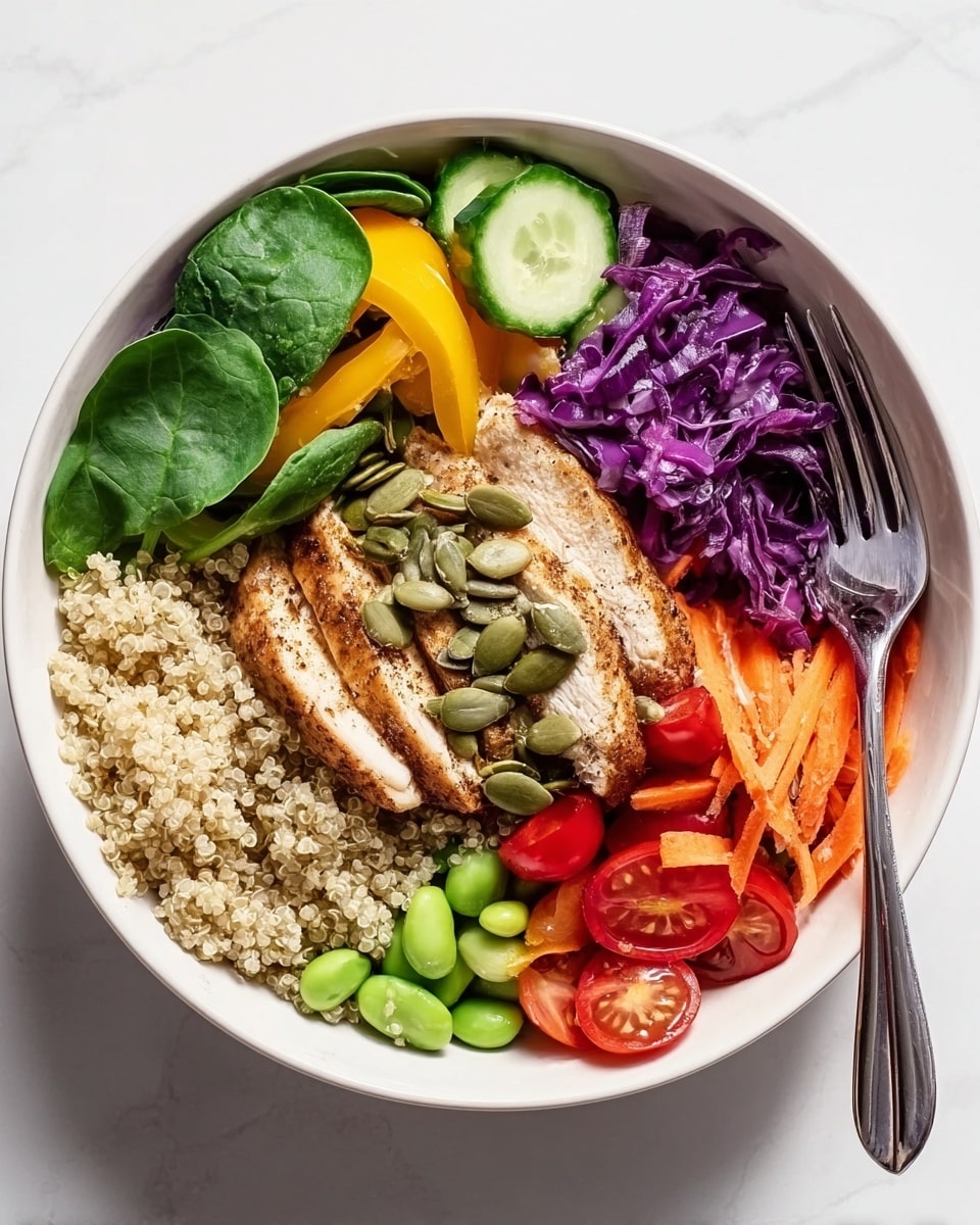A white bowl filled with layers starting from the bottom with a base of light beige quinoa. On top, there are bright green spinach leaves scattered around the edges. To the left side, thin yellow bell pepper slices are placed neatly, next to vibrant green edamame and round cucumber slices garnished with pumpkin seeds. The center layer features sliced grilled chicken breast with a light brown spice coating and more pumpkin seeds sprinkled over. The upper right section shows bright red halved cherry tomatoes beside a pile of shredded purple cabbage, followed by a small bundle of thin, orange carrot sticks tucked on the far right. The bowl sits on a white marbled surface with a silver fork partially visible on the right side. Photo taken with an iphone --ar 4:5 --v 7