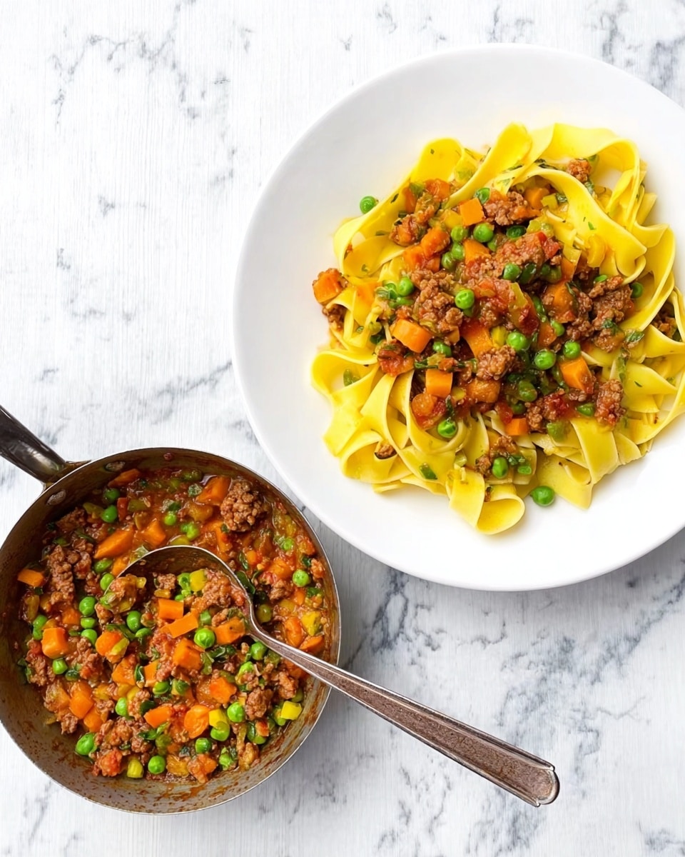 The image shows a white plate on the right with a serving of wide yellow pasta ribbons arranged in a loose pile. On top of the pasta, there is a colorful mix of small diced orange carrots, green peas, and browned meat pieces with a light red sauce that looks moist and slightly oily. To the left of the plate, there is a small metal pan filled with the same meat and vegetable mix, with a spoon resting inside. The entire scene is set on a clean white marbled surface. photo taken with an iphone --ar 4:5 --v 7