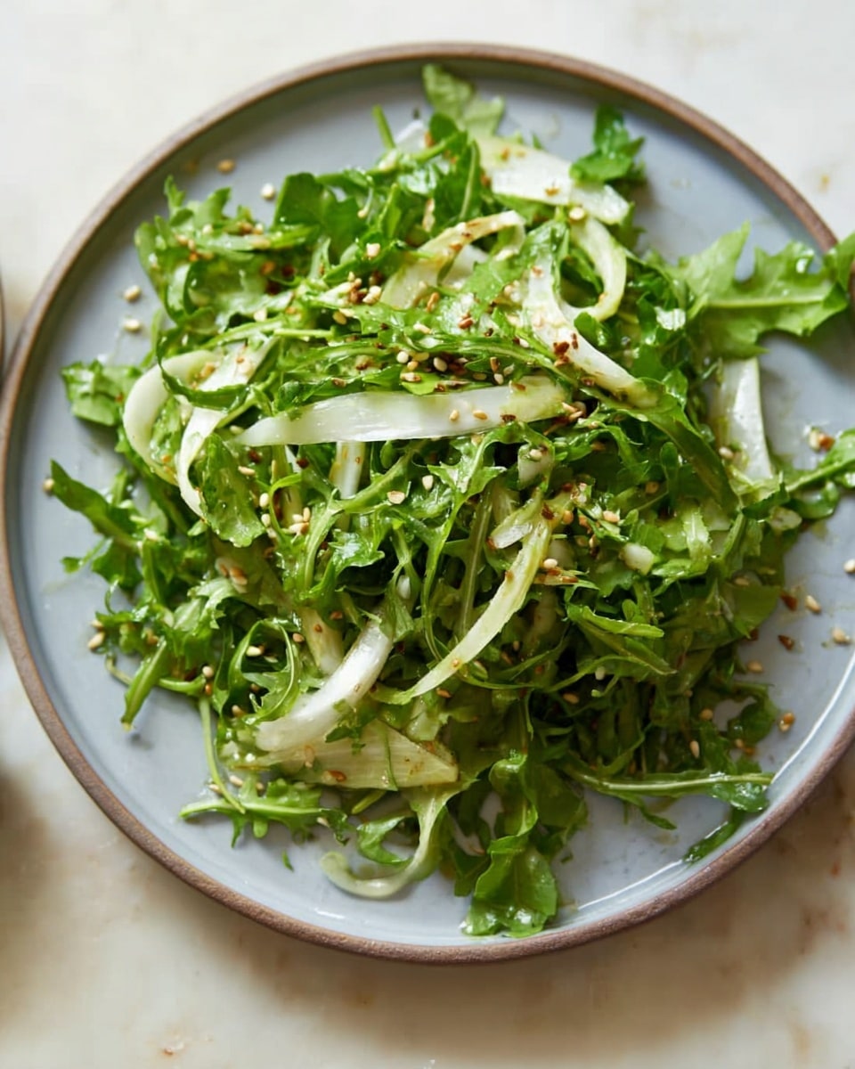 A fresh salad is shown in a white bowl with a rough texture on the outer side. The salad has two main layers: the bottom layer is a mix of bright green leafy vegetables with soft, jagged edges, and the top layer has thin, white slices of a crunchy vegetable, possibly fennel, lightly scattered on the greens. Small light brown seeds are sprinkled over the salad, and a sprinkle of black pepper is visible on top, adding small black specks. The bowl sits on a white marbled textured surface, creating a clean and fresh setting. Photo taken with an iphone --ar 4:5 --v 7