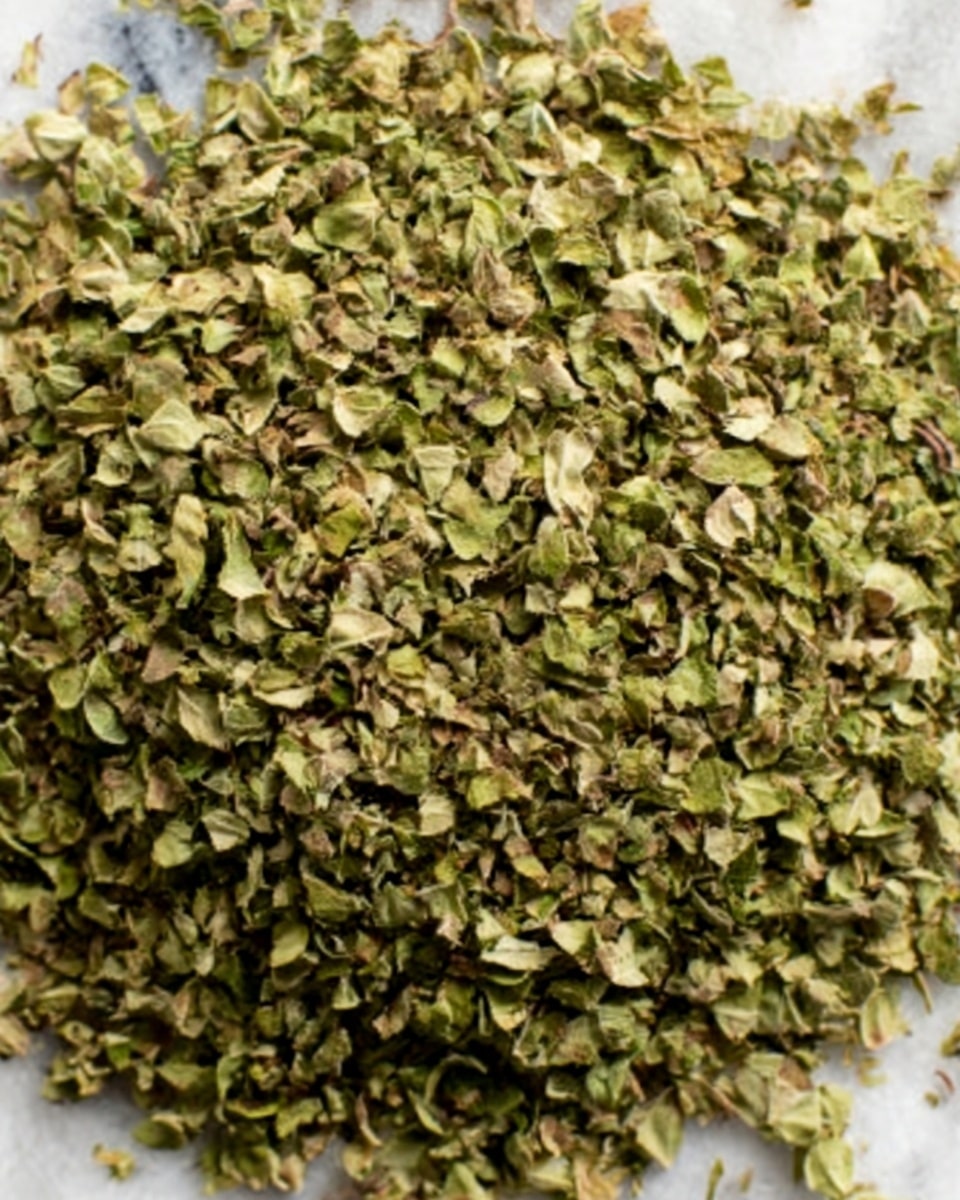 The image shows a close-up view of a large amount of small, dried green leaves piled closely together. The leaves have a rough texture with some small stems mixed in, giving a natural, slightly uneven look. The green color varies slightly between bright and dull shades, highlighting the dryness and crispness of the leaves. The image is focused tightly on the leaves, filling the whole frame, with no visible container or background, just the detailed texture of the dried greens. photo taken with an iphone --ar 4:5 --v 7